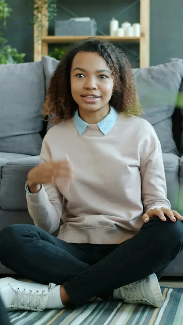 Original frame: a young woman vlogs sitting on the living-room floor