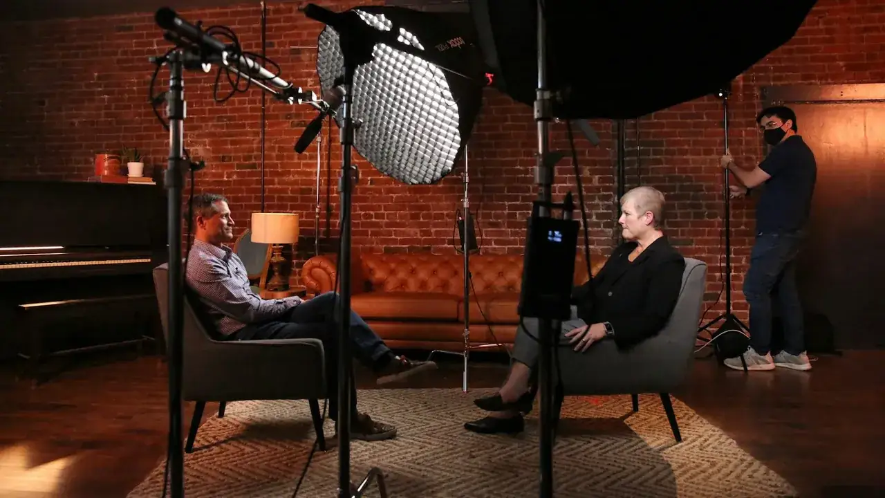 A studio interview: two people in armchairs in front of a camera